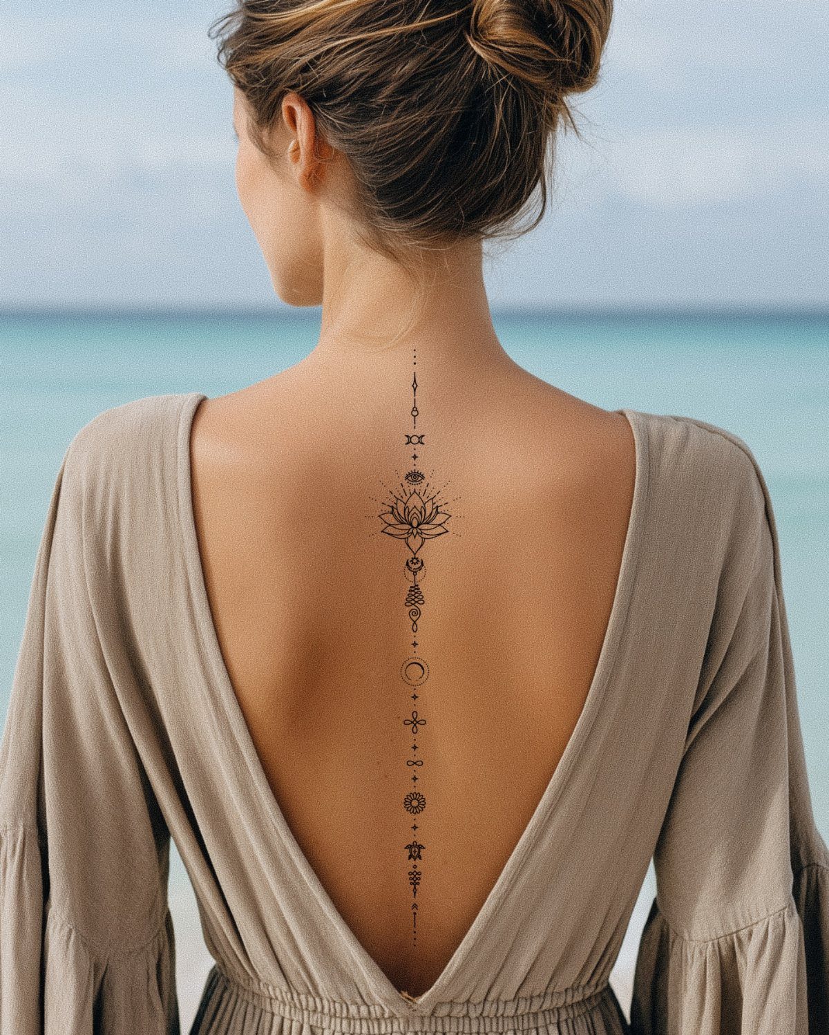 Vertical lotus flower and symbol tattoo on a woman's back by the ocean