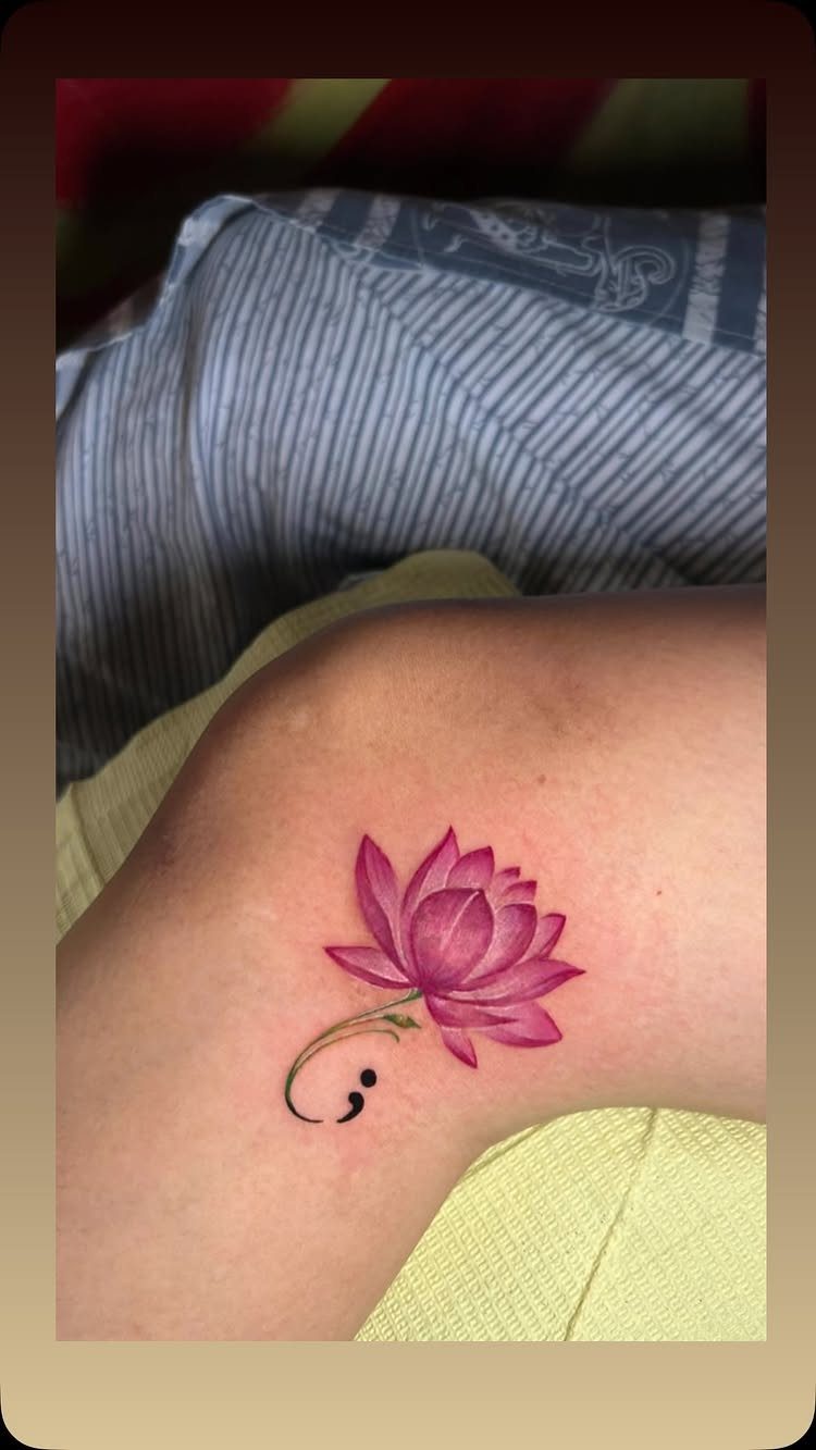 Pink lotus flower tattoo with a black semicolon integrated into the stem.
