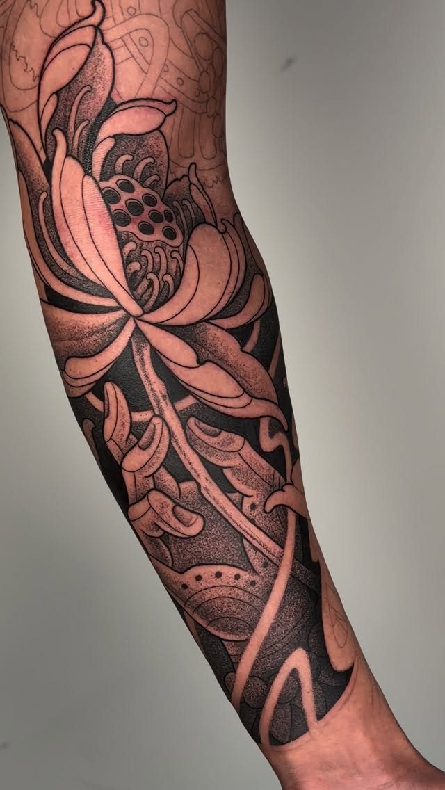 Detailed black and grey lotus flower tattoo wrapping around a person's forearm