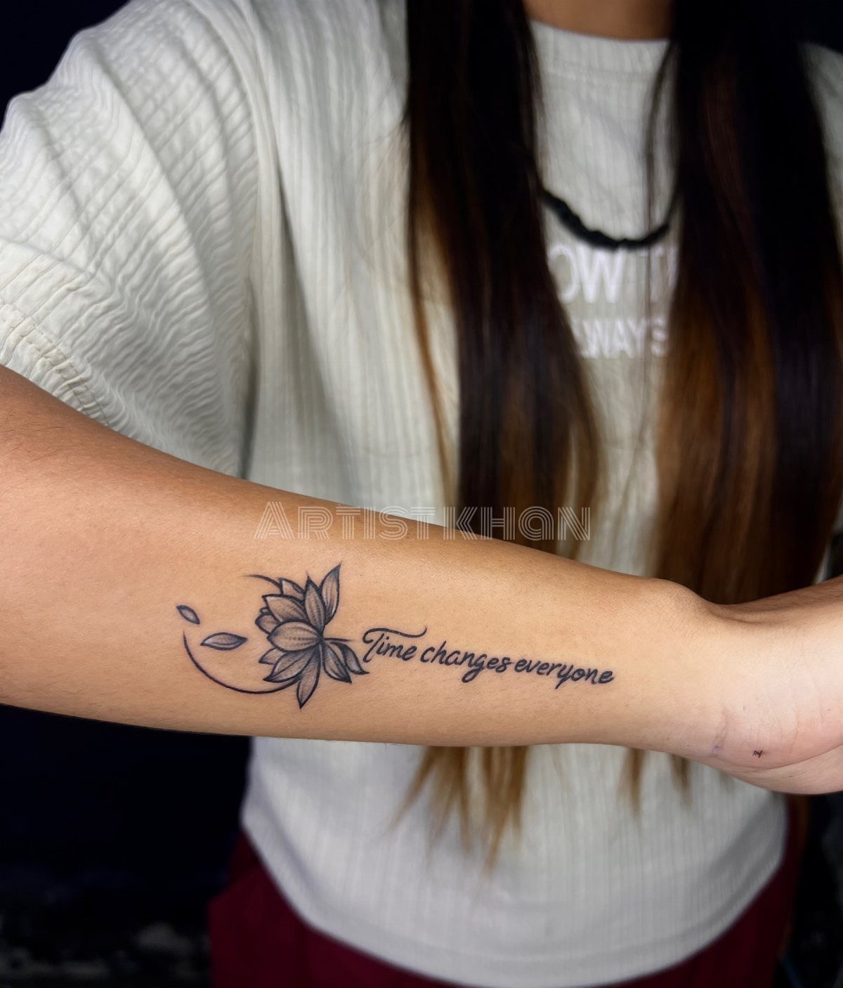 Lotus flower tattoo with cursive script text on a person's inner forearm