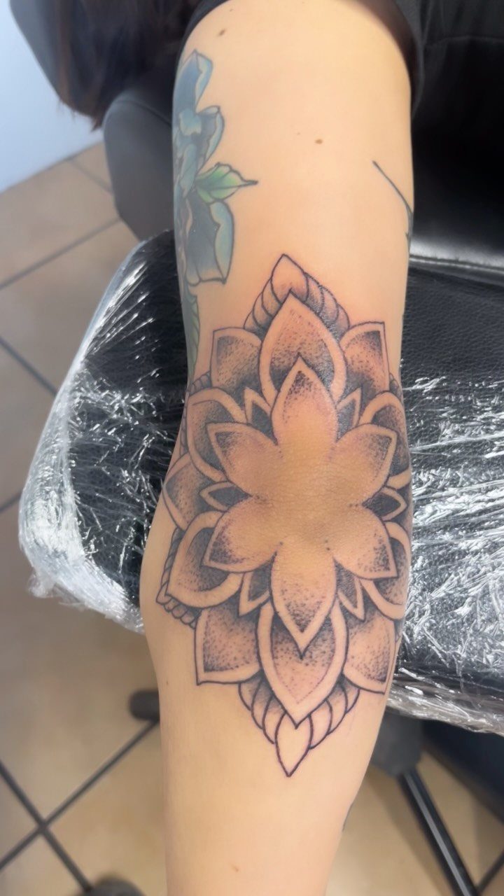 Mandala lotus flower tattoo with symmetrical shading on a person's elbow