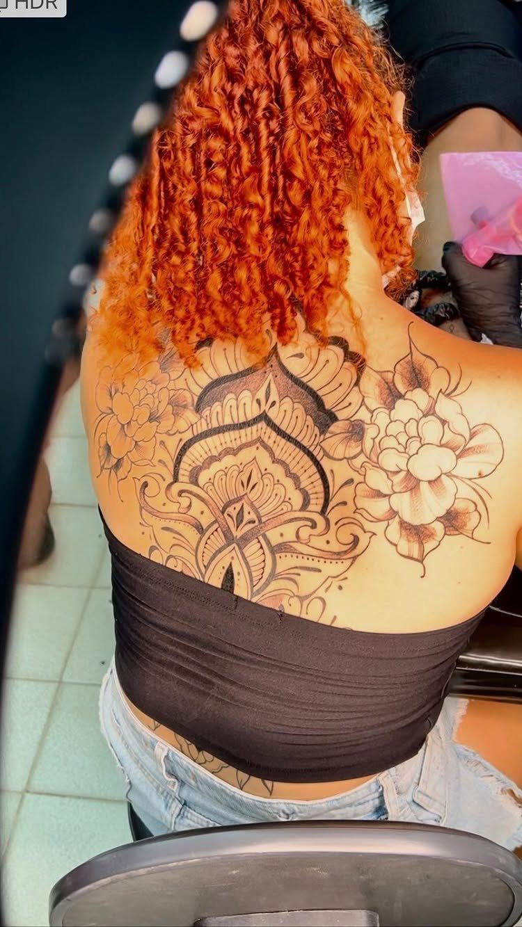 Large ornamental lotus flower tattoo on a woman's upper back with red hair.