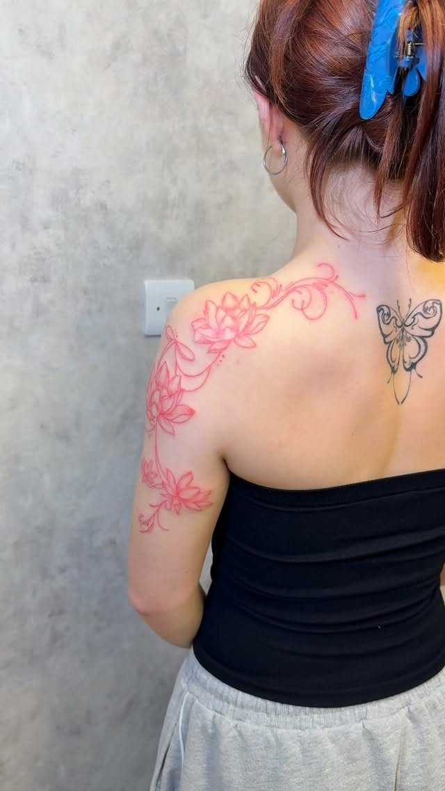 Pink lotus flower tattoo with vines on a woman's shoulder and upper back