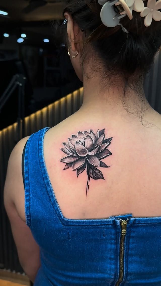 Detailed black and grey lotus flower tattoo on a person's upper back