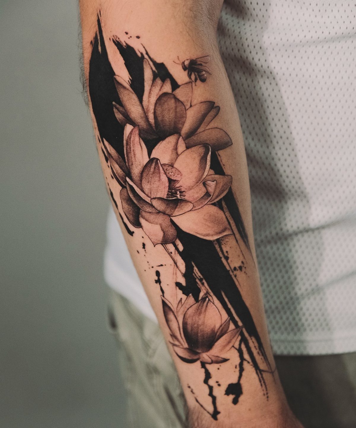 Shaded lotus flower tattoo with black ink splashes on a person's forearm