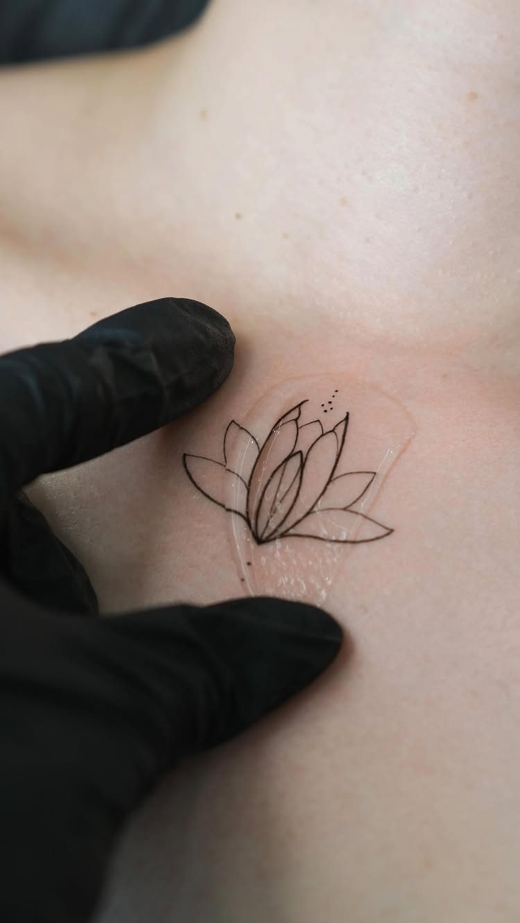 Small black ink lotus flower tattoo on skin covered by clear protective film