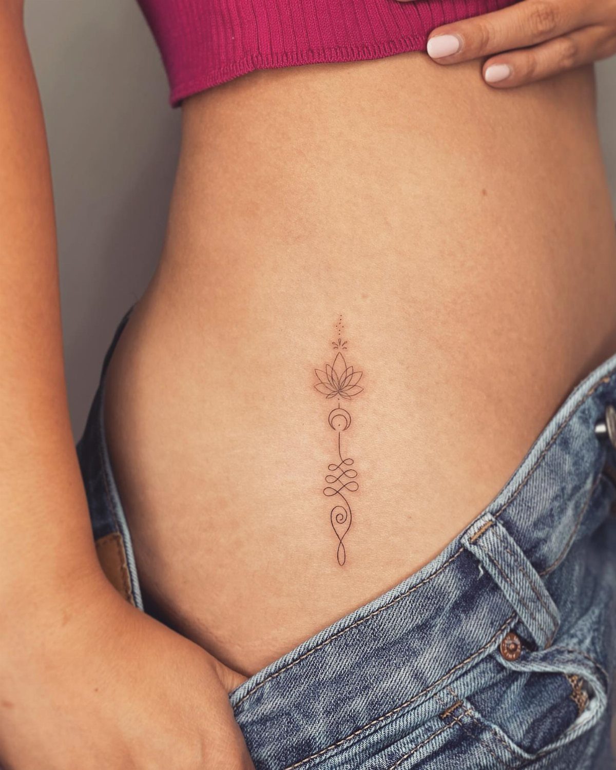 Unalome lotus tattoo with a crescent moon on a person's lower abdomen.