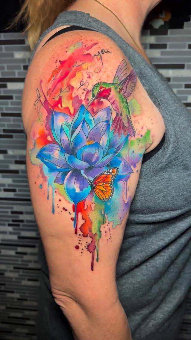 Watercolor tattoo of a blue lotus flower with a hummingbird and butterfly on arm
