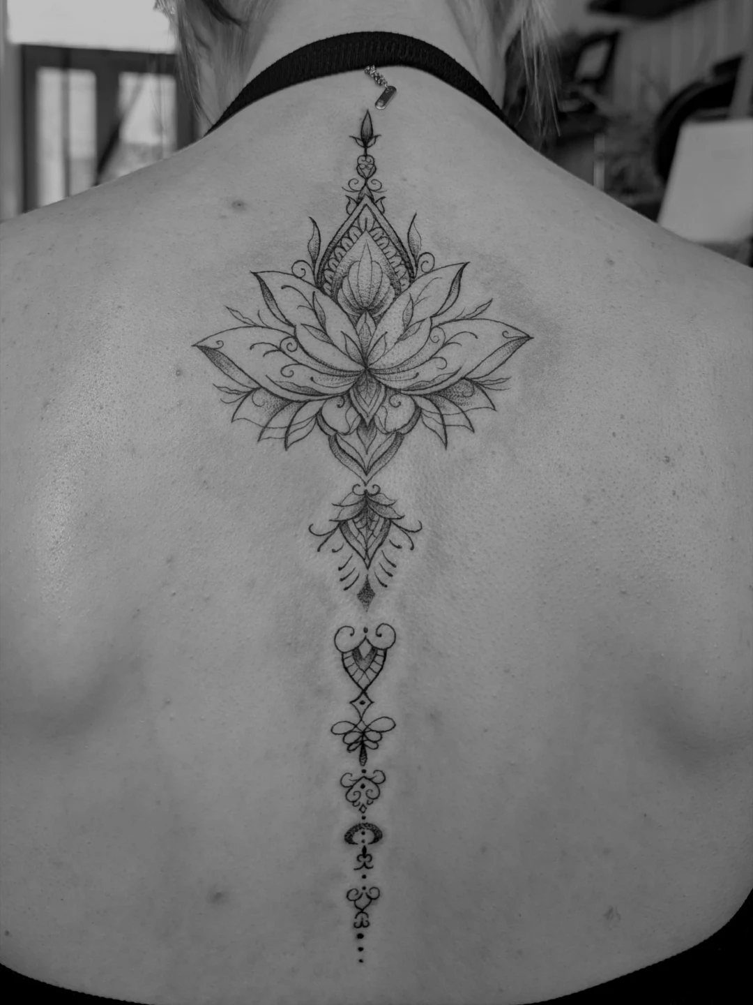 Lotus mandala tattoo centered on the upper back and spine of a person.