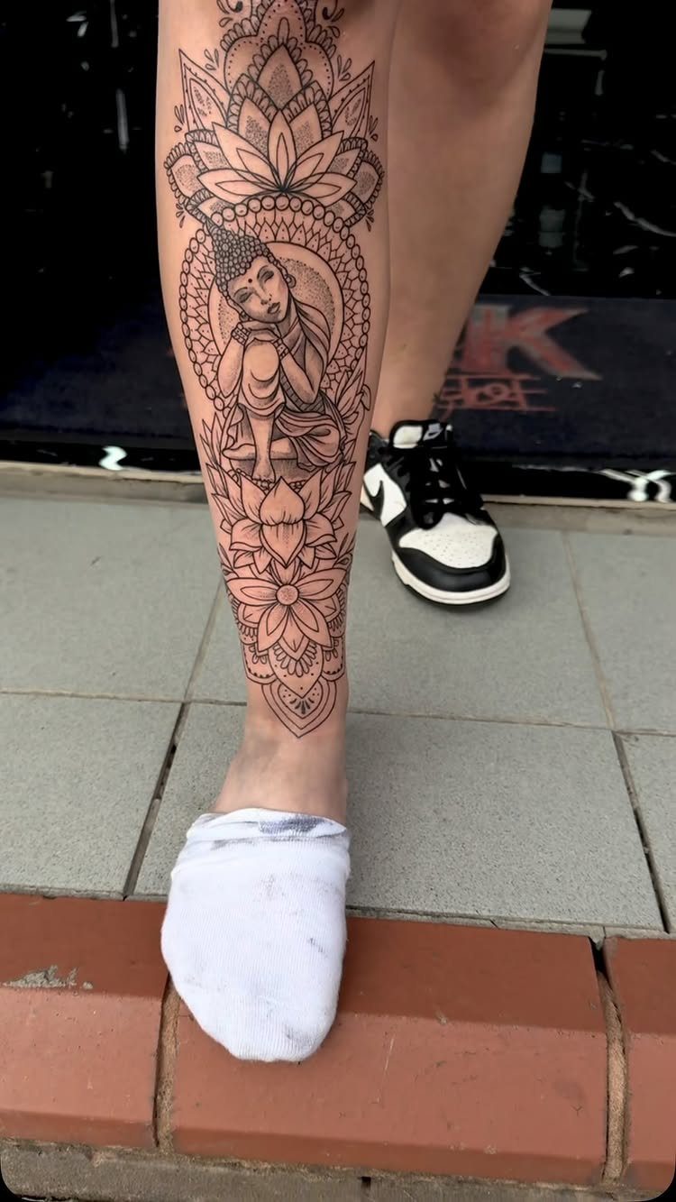 Buddha figure centered in an intricate lotus mandala tattoo on a lower leg