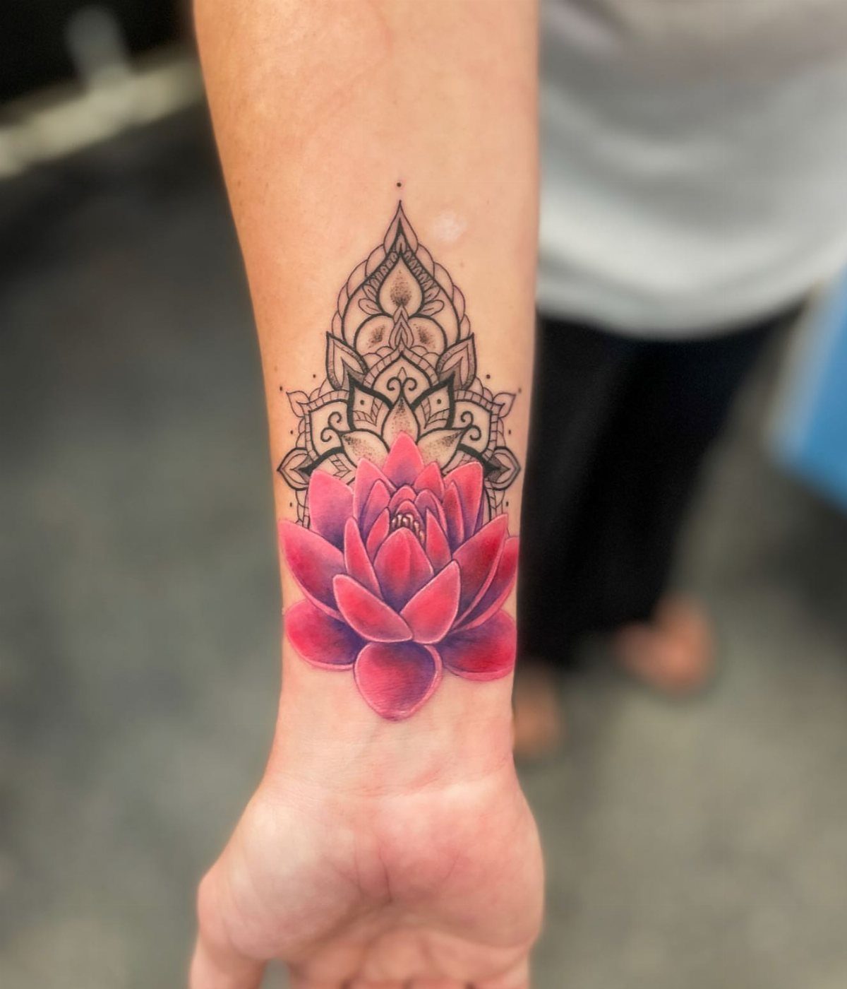 Lotus flower tattoo with a black geometric mandala on a person's forearm