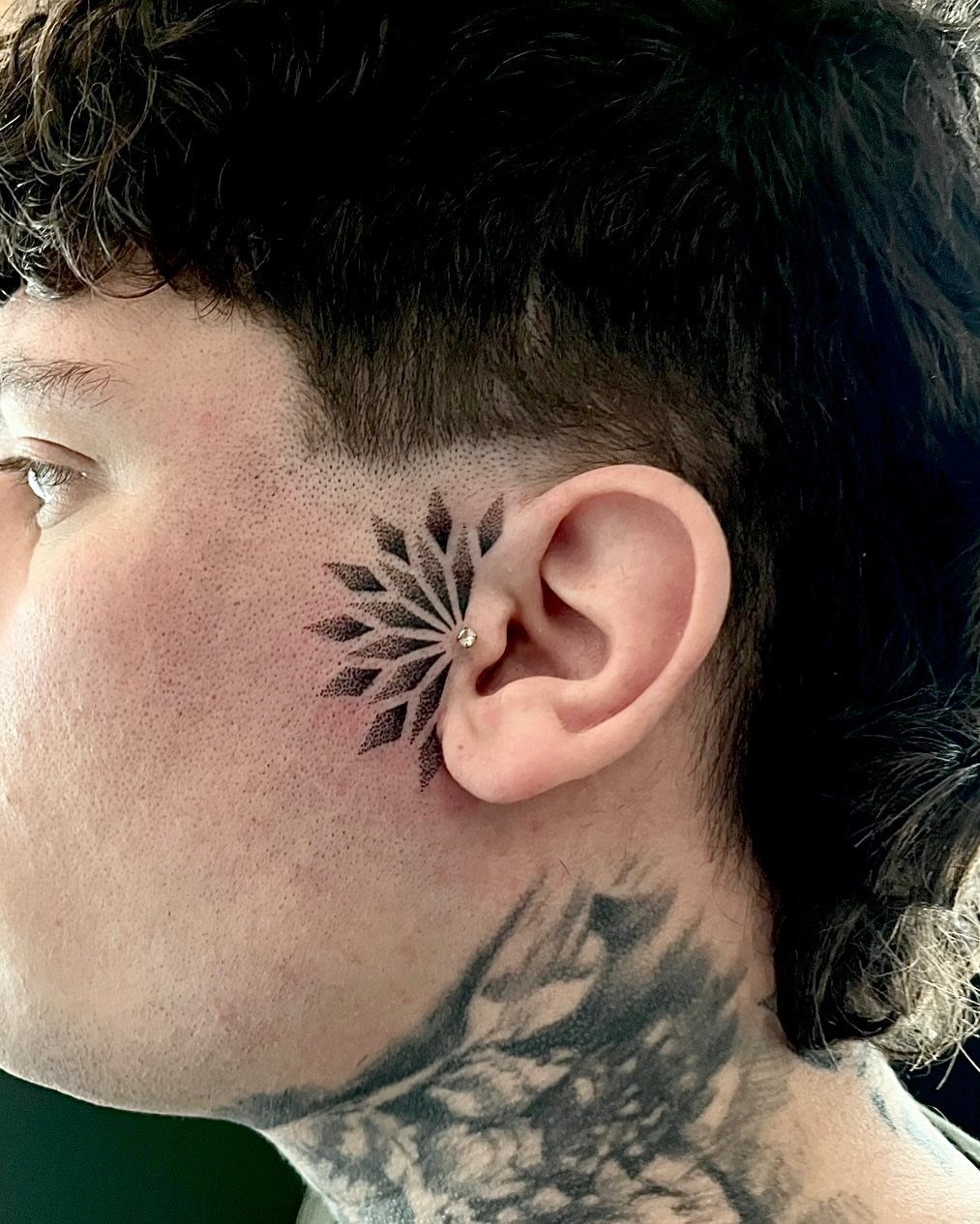 Lotus mandala tattoo behind the ear of a person with neck tattoos.