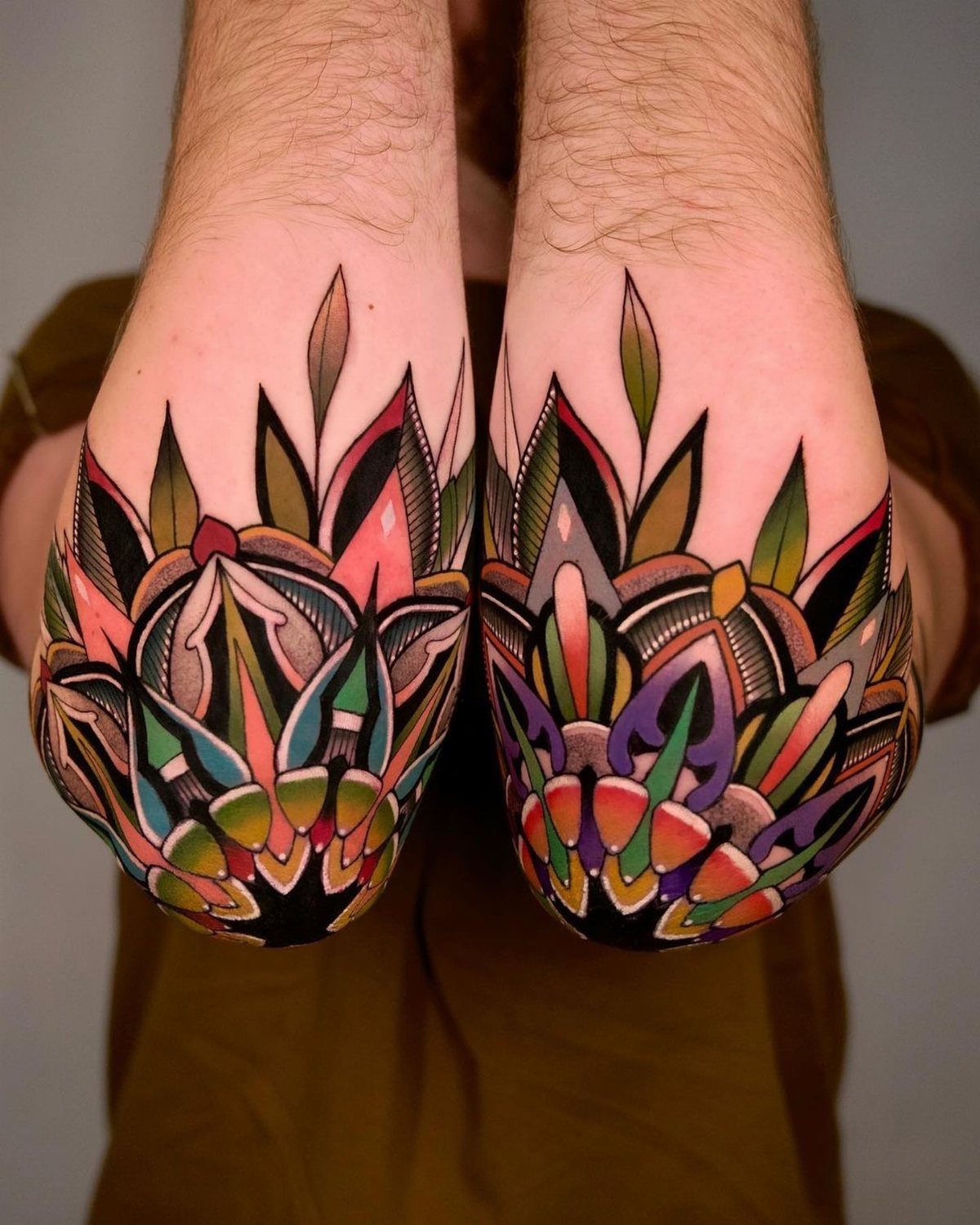 Colorful lotus mandala tattoos on both elbows of a person's arms.