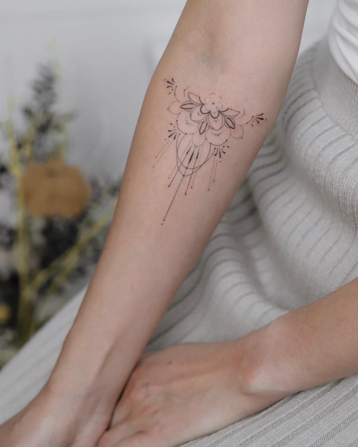 Half-lotus mandala tattoo with fine lines and dots on a person's forearm