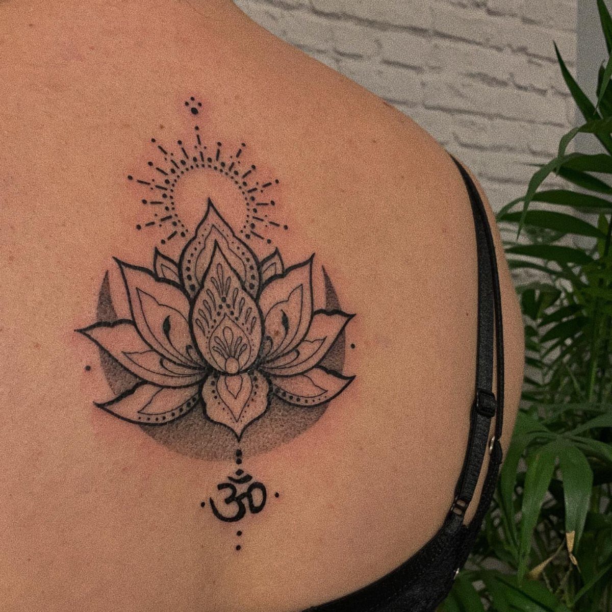 Lotus flower mandala tattoo on a shoulder with an Aum symbol below.