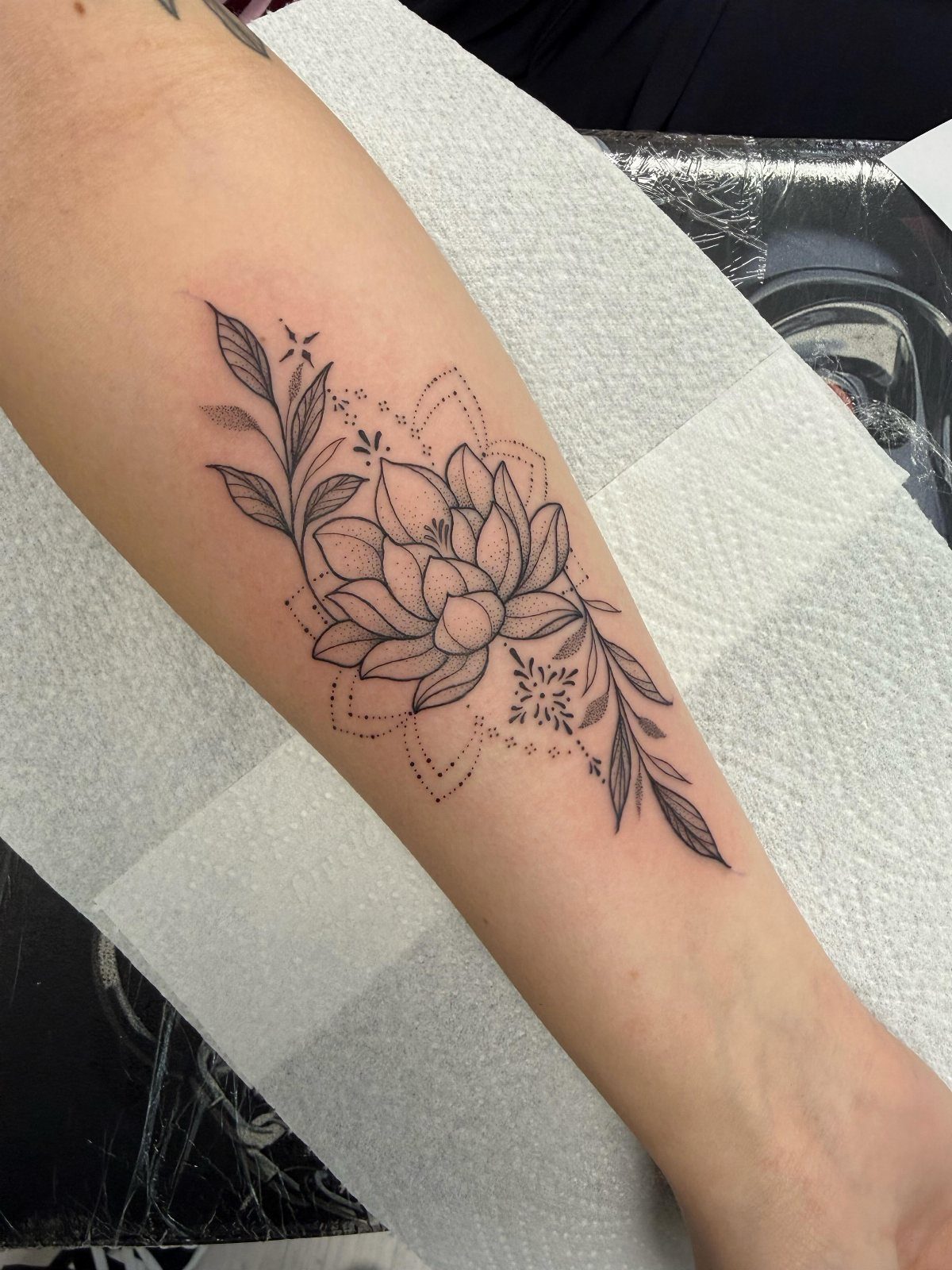 Lotus flower mandala tattoo with leafy vines on a person's forearm