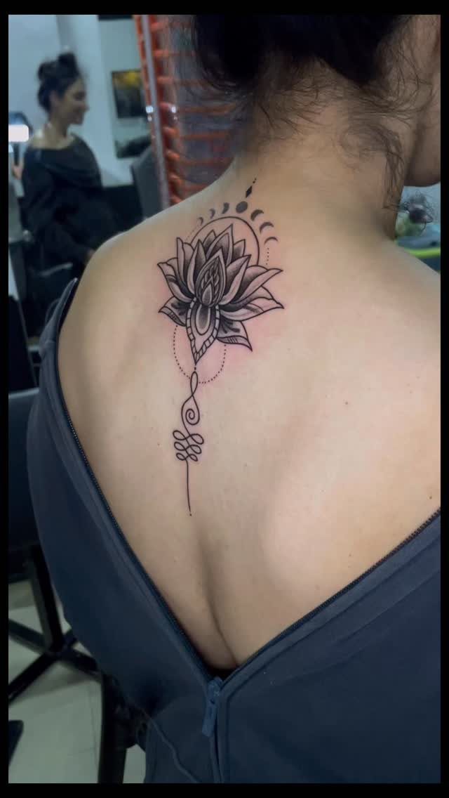 Lotus flower mandala tattoo with an unalome symbol on a person's upper back