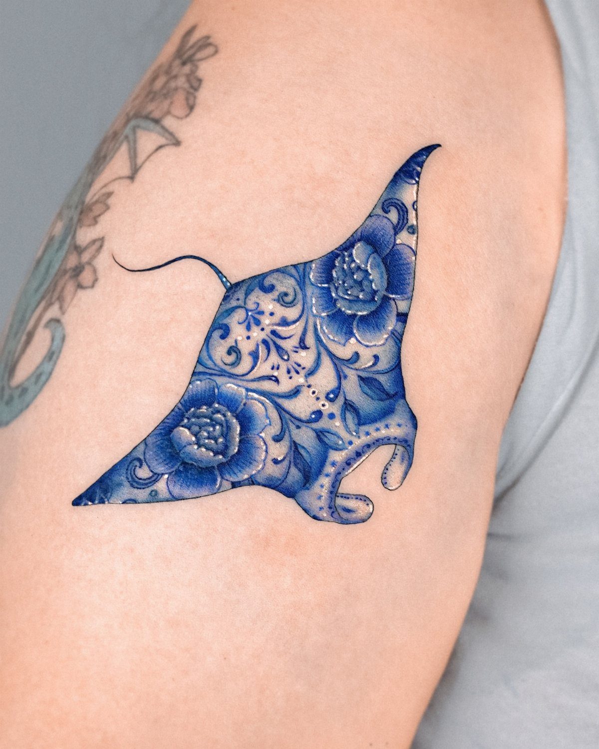 Blue manta ray tattoo with floral patterns on a person's shoulder