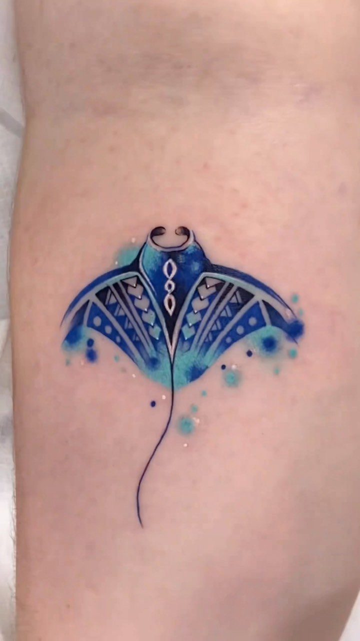 Bright blue manta ray tattoo with tribal patterns on a person's skin.