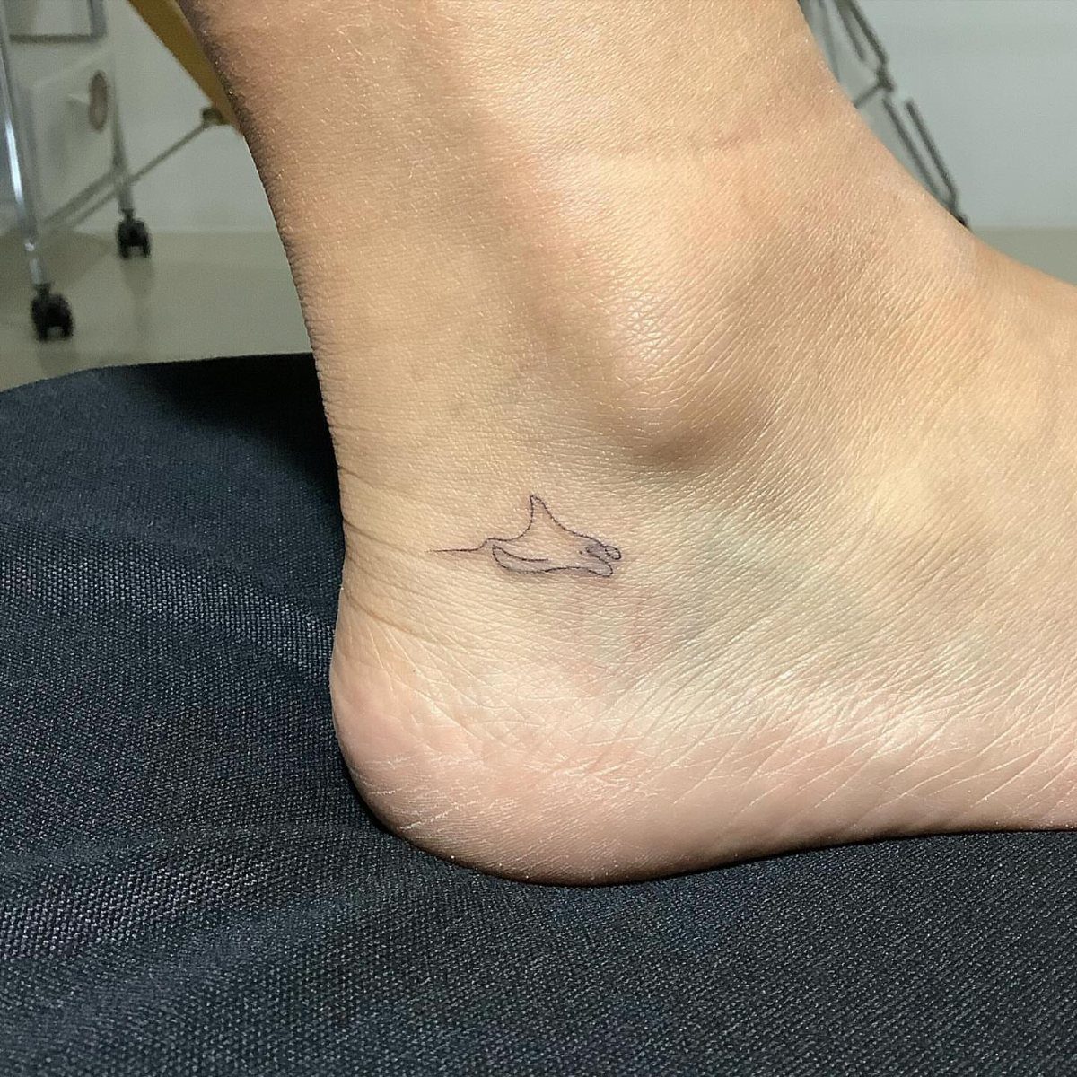 Small black ink manta ray tattoo on the side of a person's ankle.