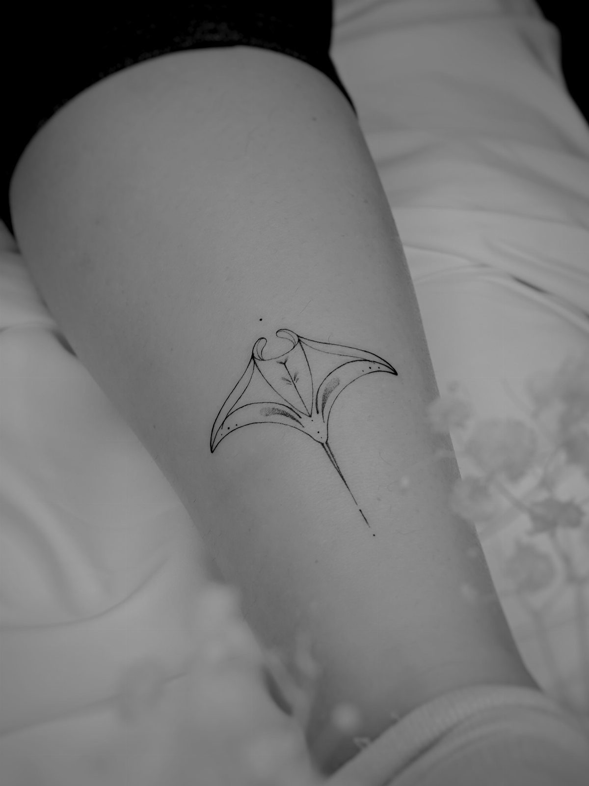 Manta ray line-art tattoo on a person's forearm in black and white.