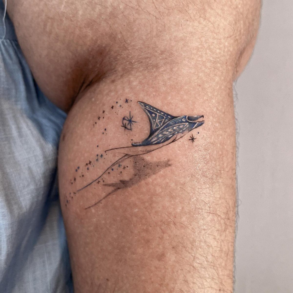 Manta ray tattoo with tribal motifs and stars in blue ink on an arm