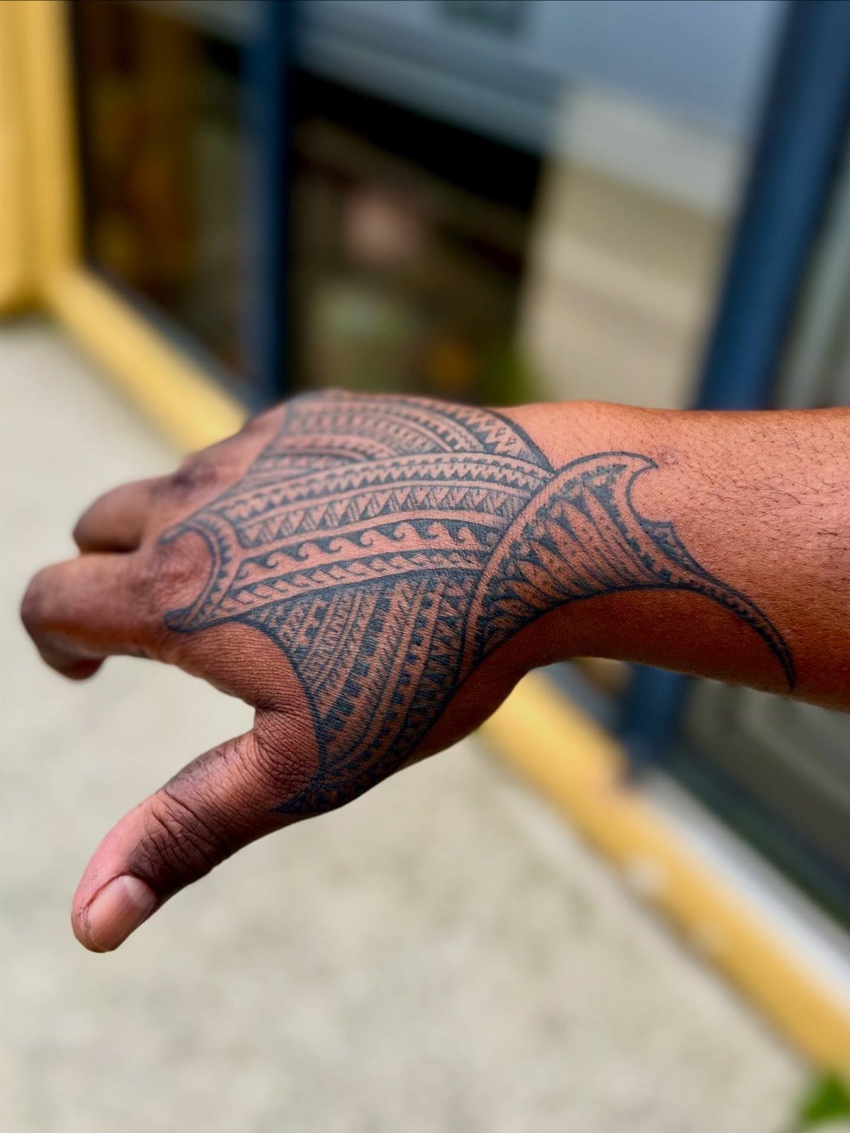 Tribal manta ray tattoo covering the back of a person's hand and wrist.