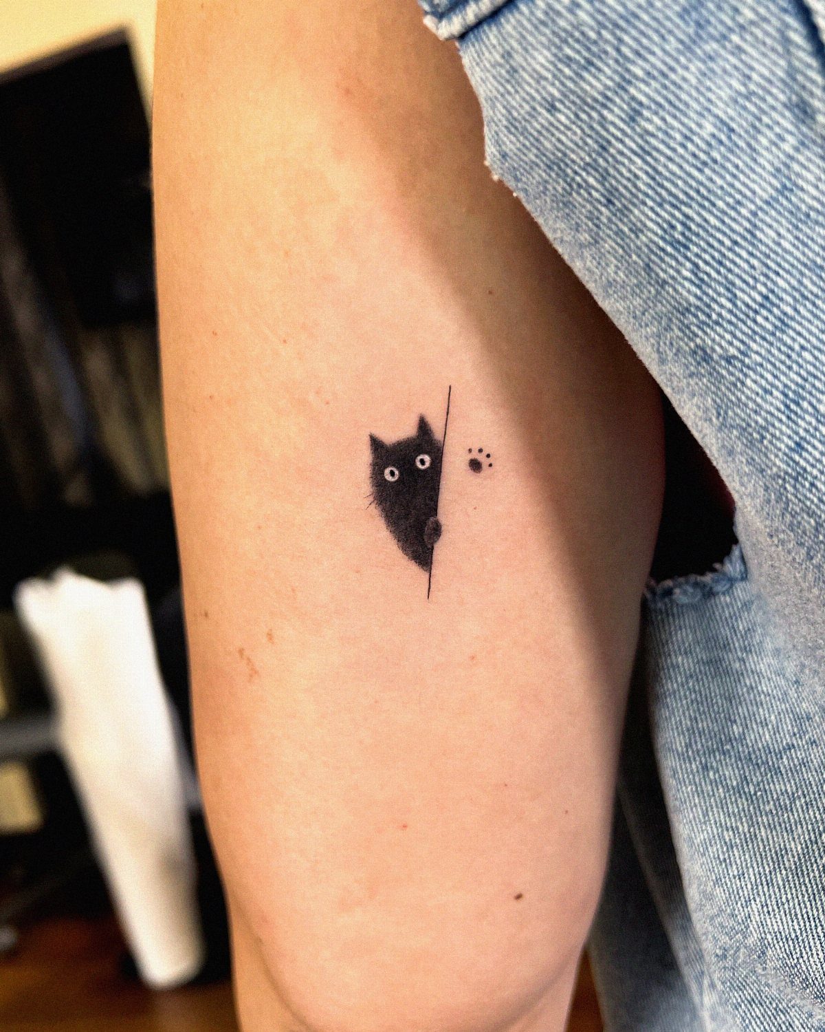 Small black cat tattoo peeking from behind a line on an arm