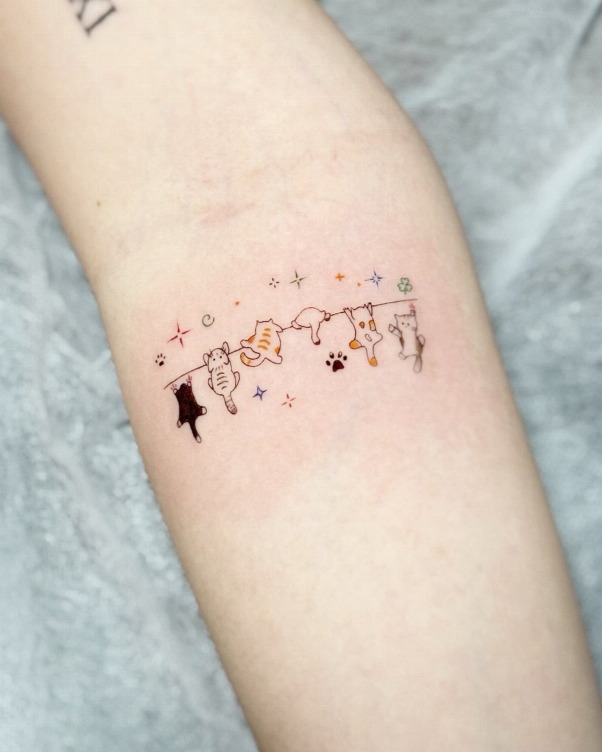 Small tattoo of several relaxed cats lounging on a line on a person's arm.