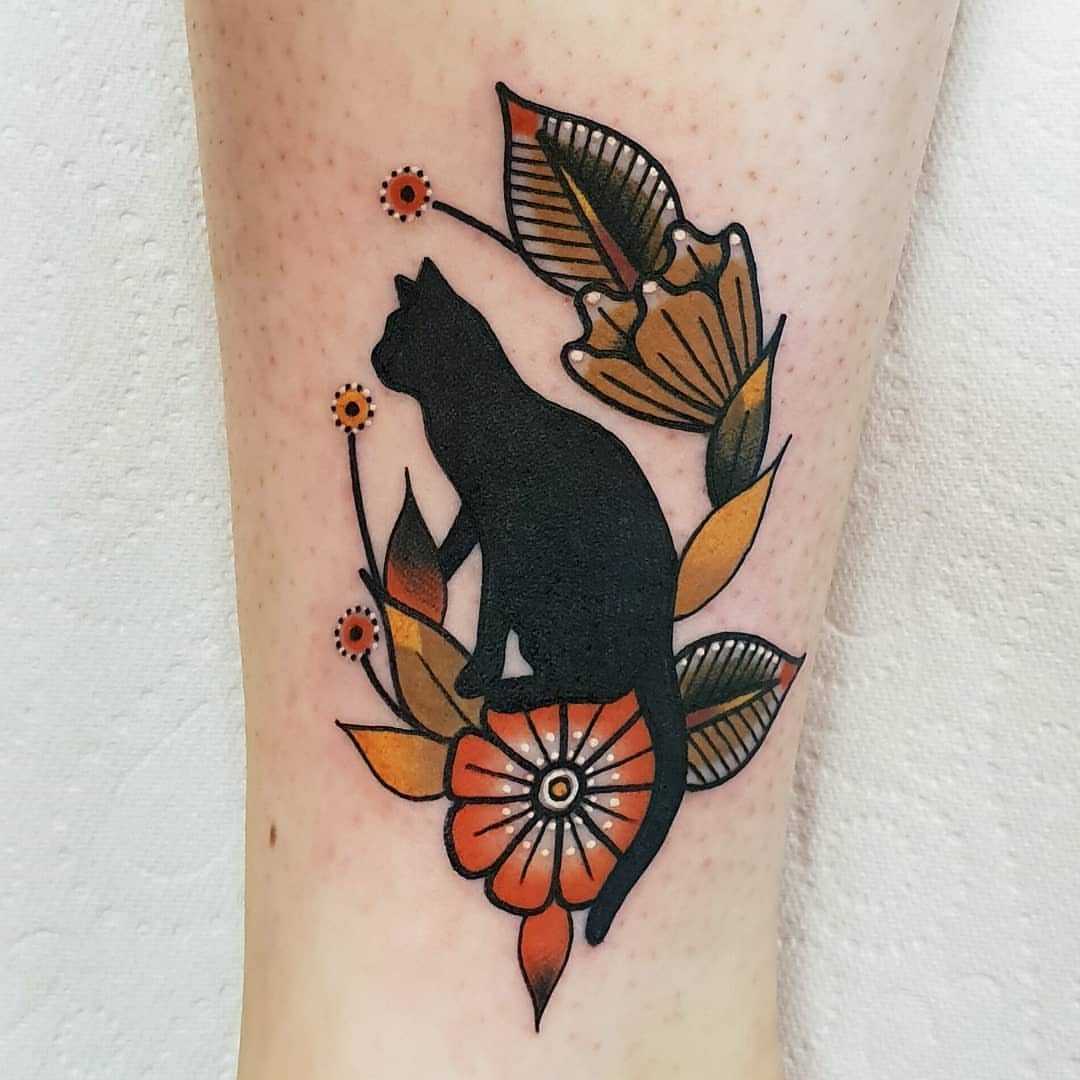 Black silhouette cat tattoo surrounded by orange flowers and green leaves on skin