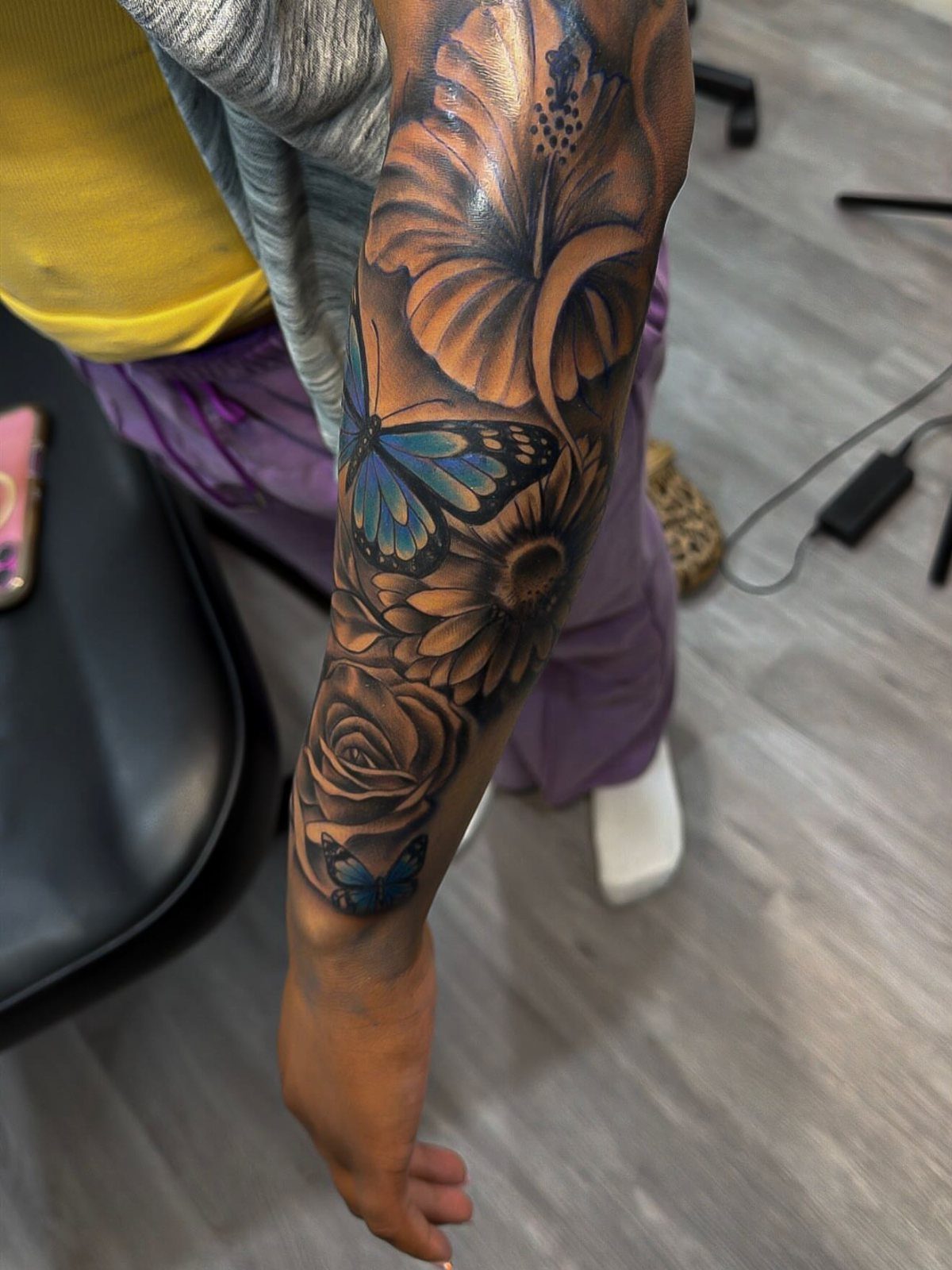 Blue butterfly and flower tattoos on a person's forearm with detailed shading.