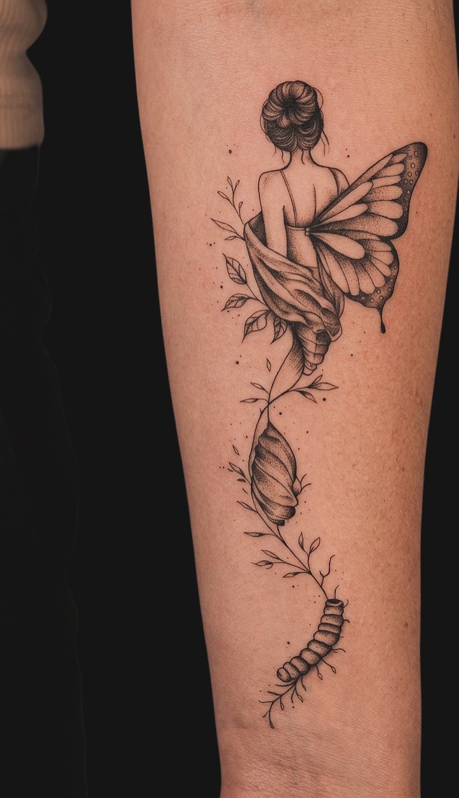 Tattoo on an arm showing a caterpillar, chrysalis, and woman with butterfly wings.