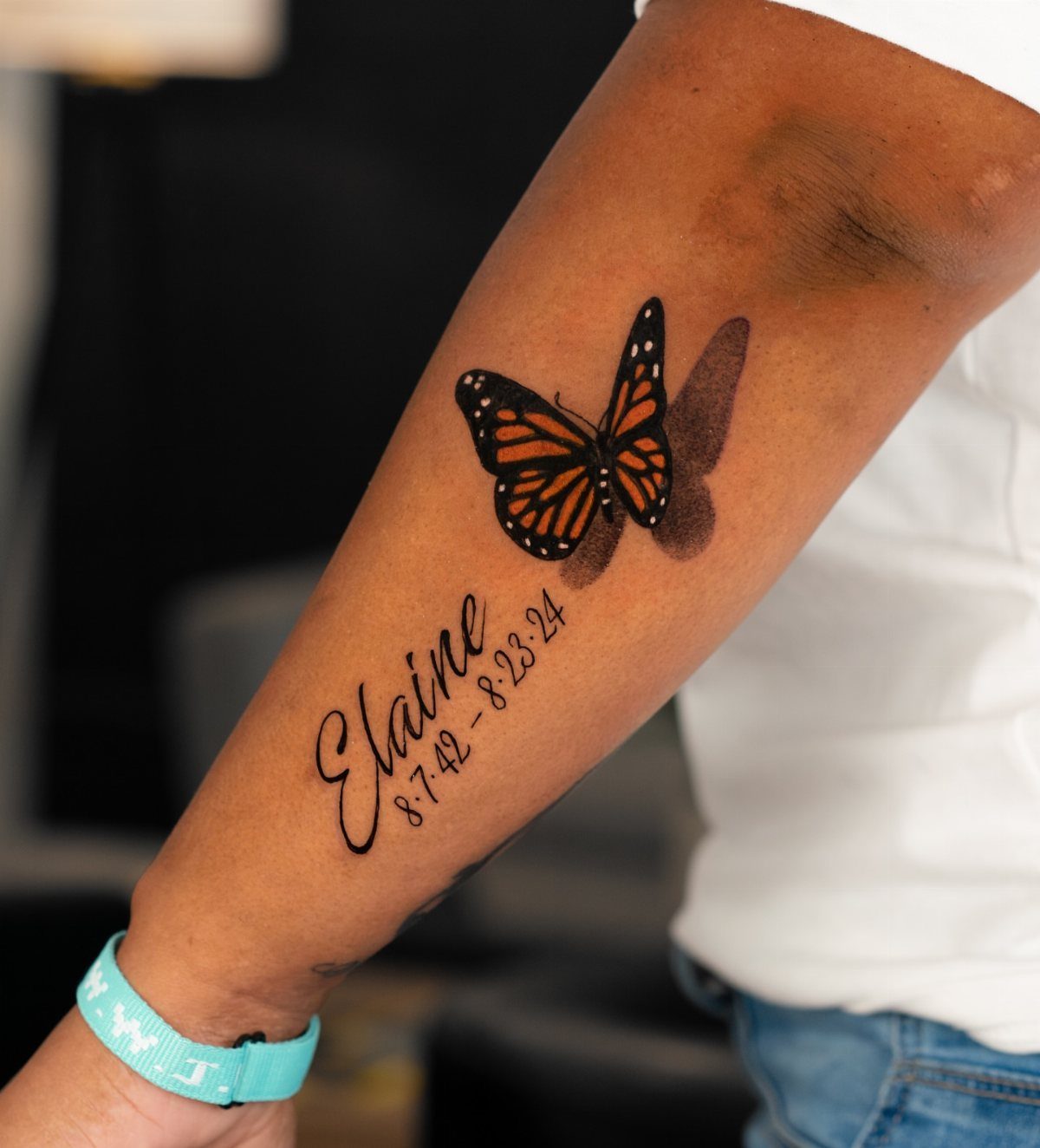 Monarch butterfly tattoo with a name and dates on a person's forearm.