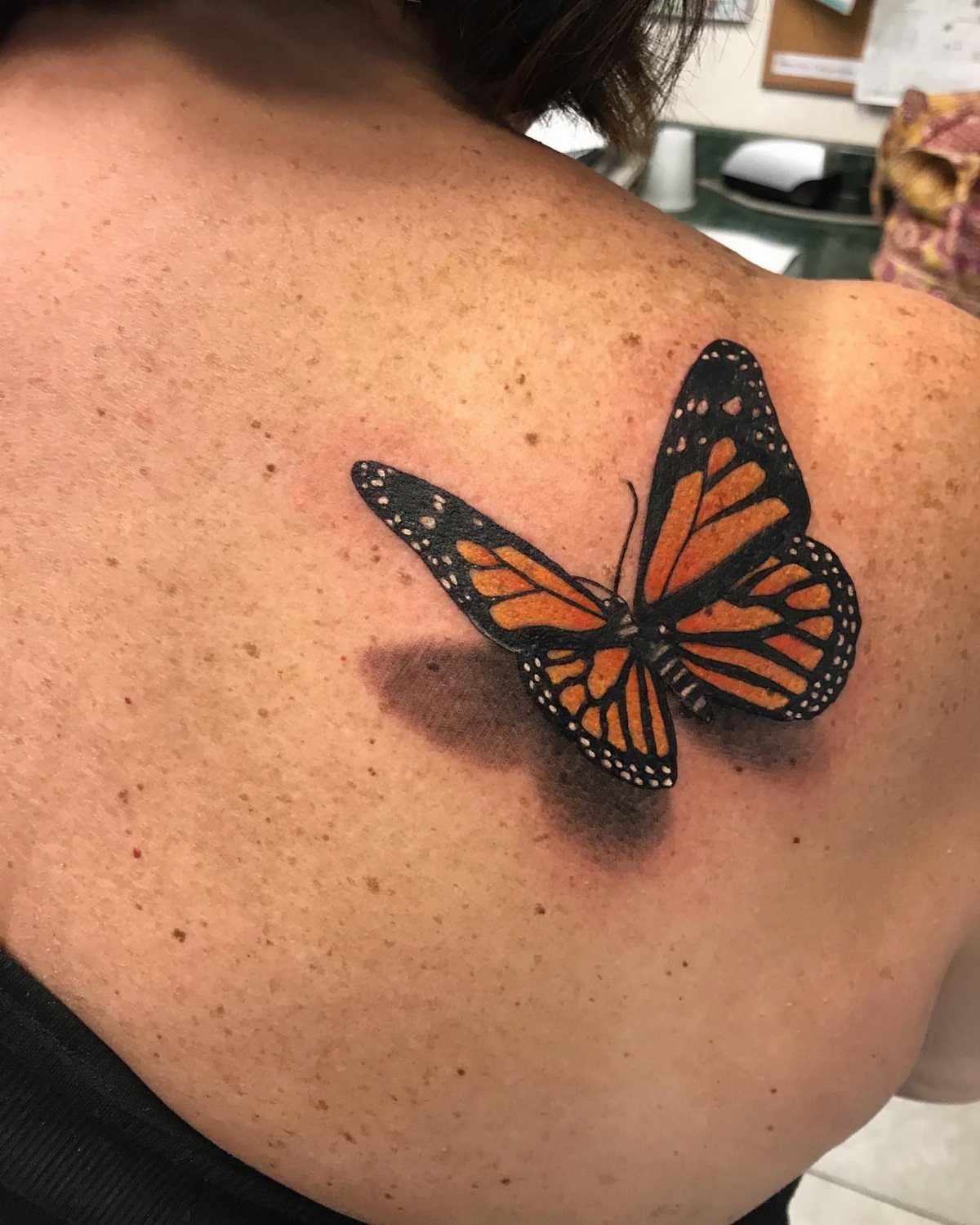 Monarch butterfly tattoo with 3D shading on a person's upper back.