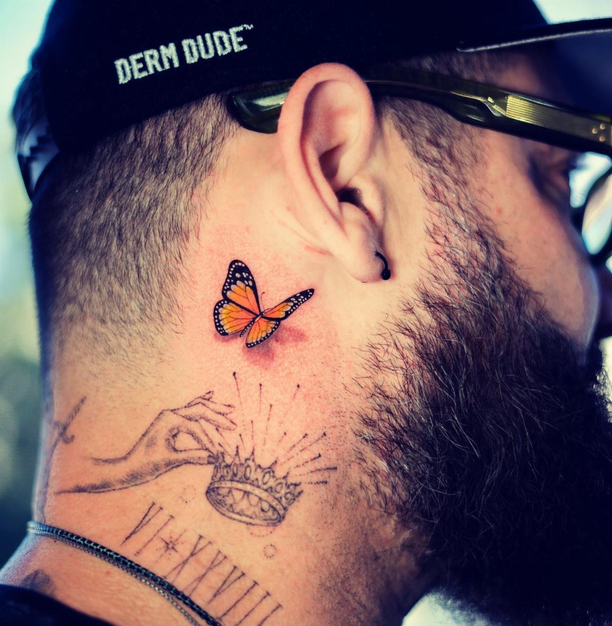 Monarch butterfly tattoo on a man's neck above a crown tattoo.