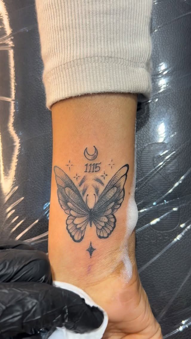 Butterfly tattoo on a wrist featuring a crescent moon and small stars.