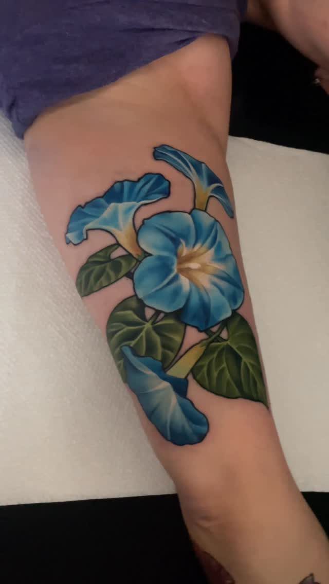 Blue trumpet-shaped morning glory flower tattoo on a person's lower leg