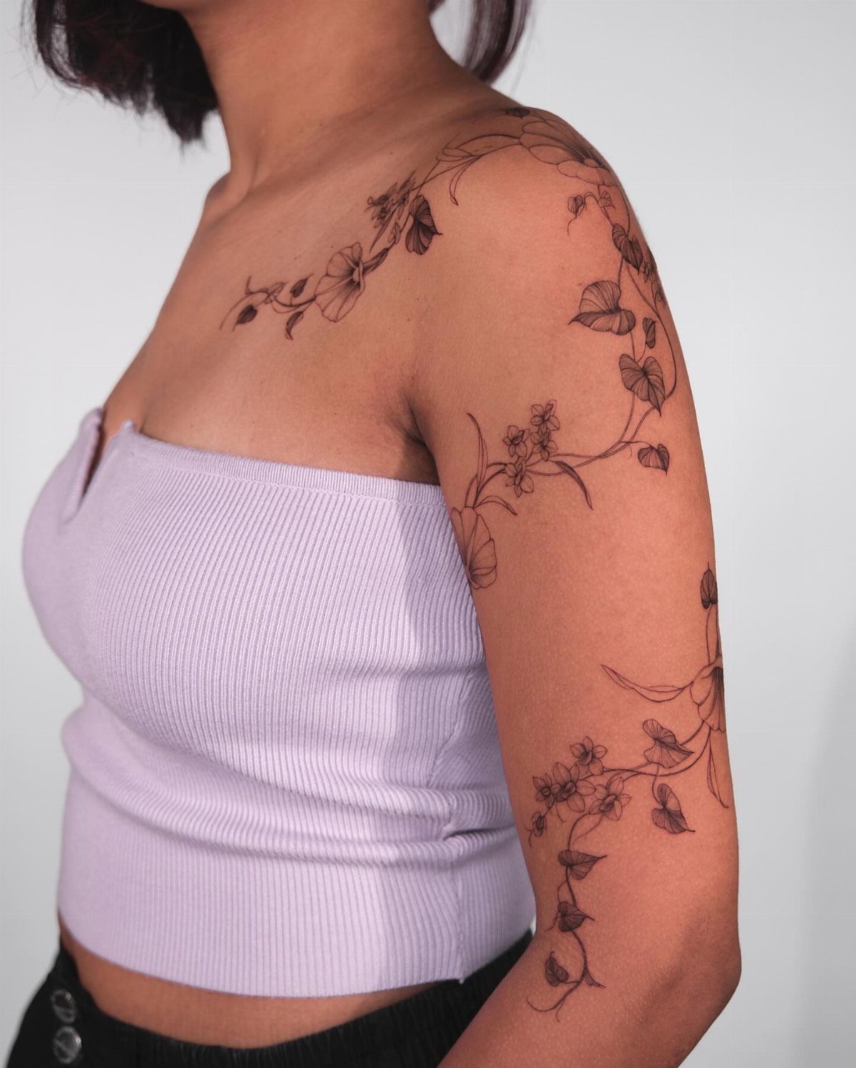 Cascading morning glory flower tattoo in black ink on a person's shoulder and arm