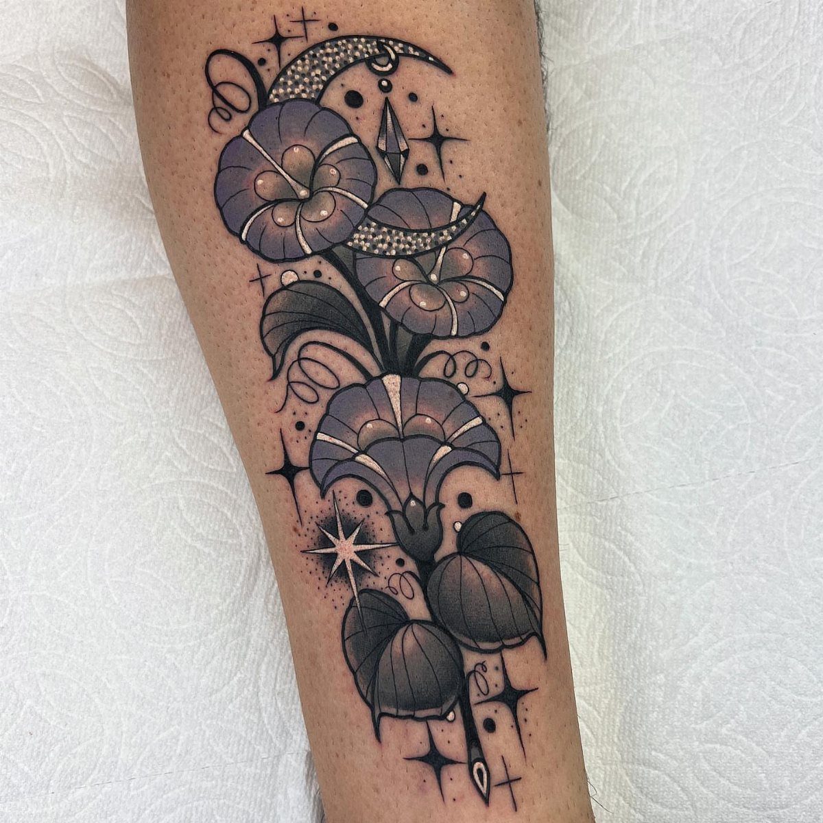 Purple morning glory flower tattoo with crescent moons and stars on an arm