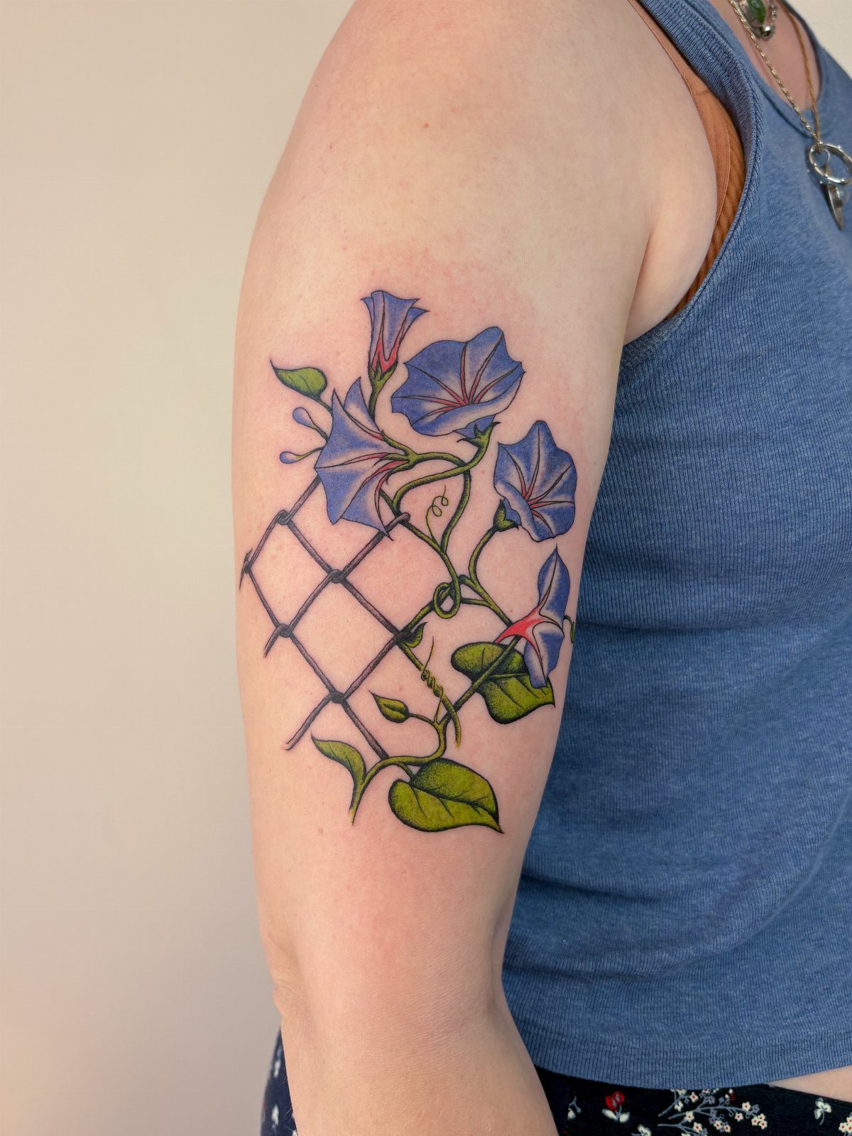 Blue morning glory flower tattoo climbing a black trellis on an arm