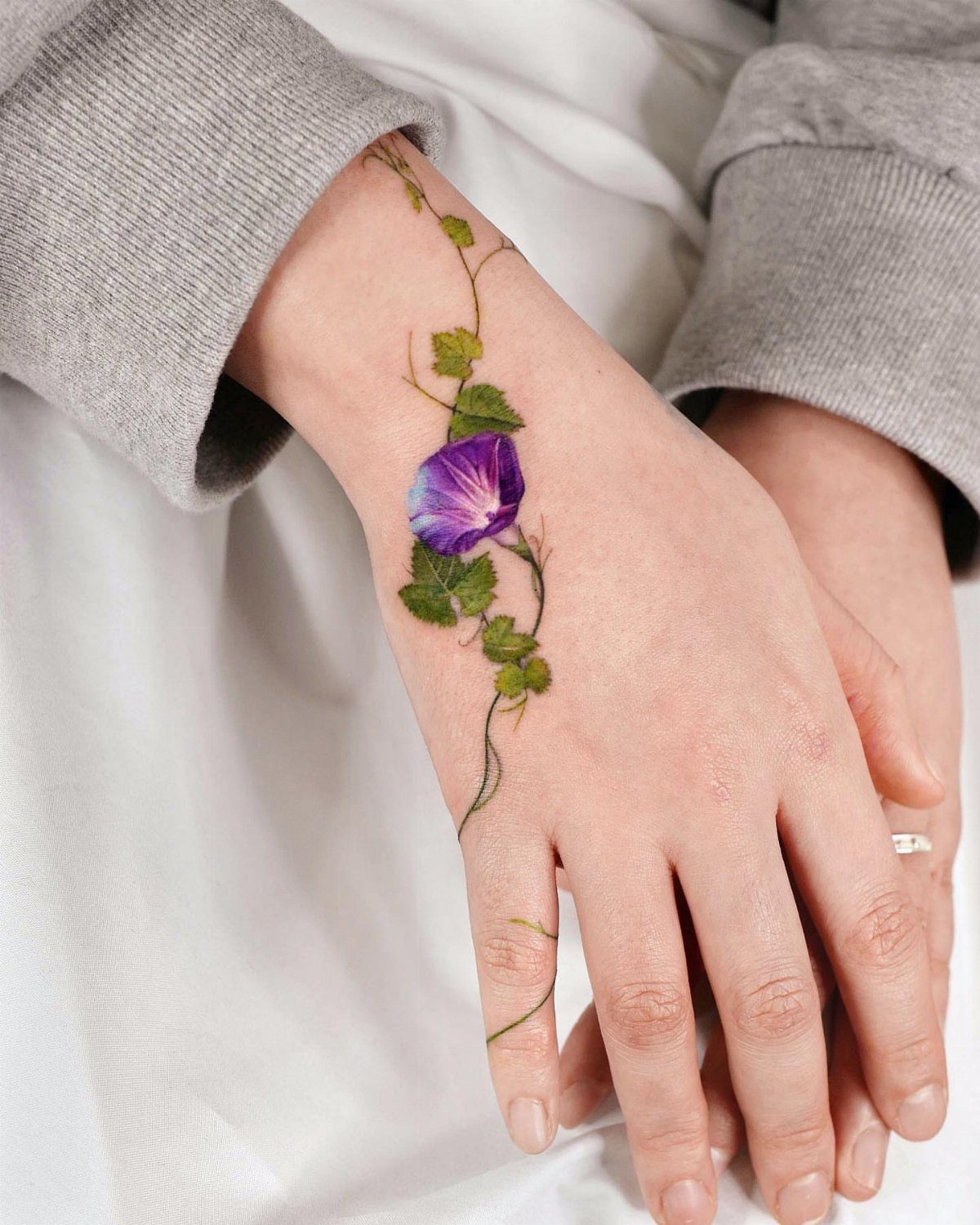 Purple morning glory flower tattoo with green vine winding down a person's hand