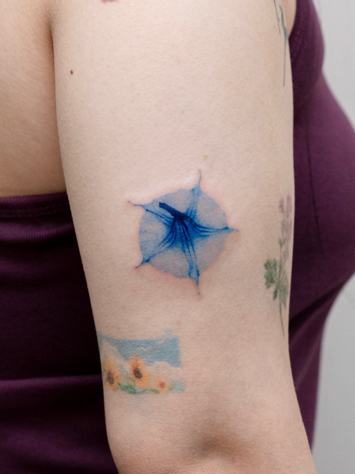 Blue watercolor morning glory flower tattoo on a person's upper arm