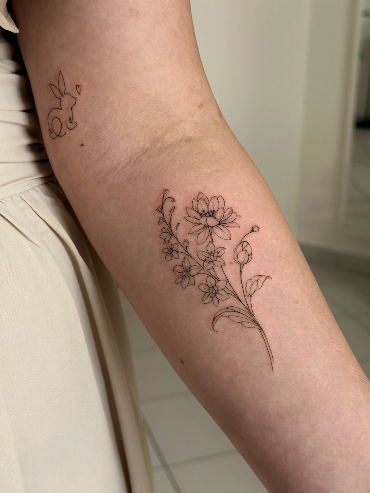 Floral tattoo of cosmos and marigolds on a person's forearm in black ink