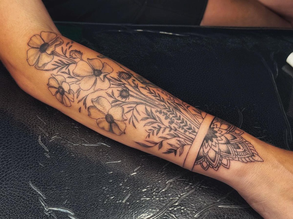 Black ink cosmos flower and mandala tattoo on a person's forearm