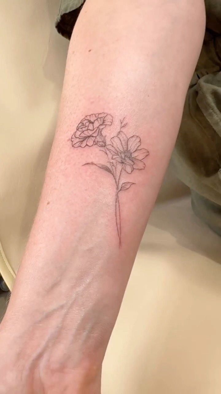 Cosmos flower tattoo with fine black lines on a person's forearm.