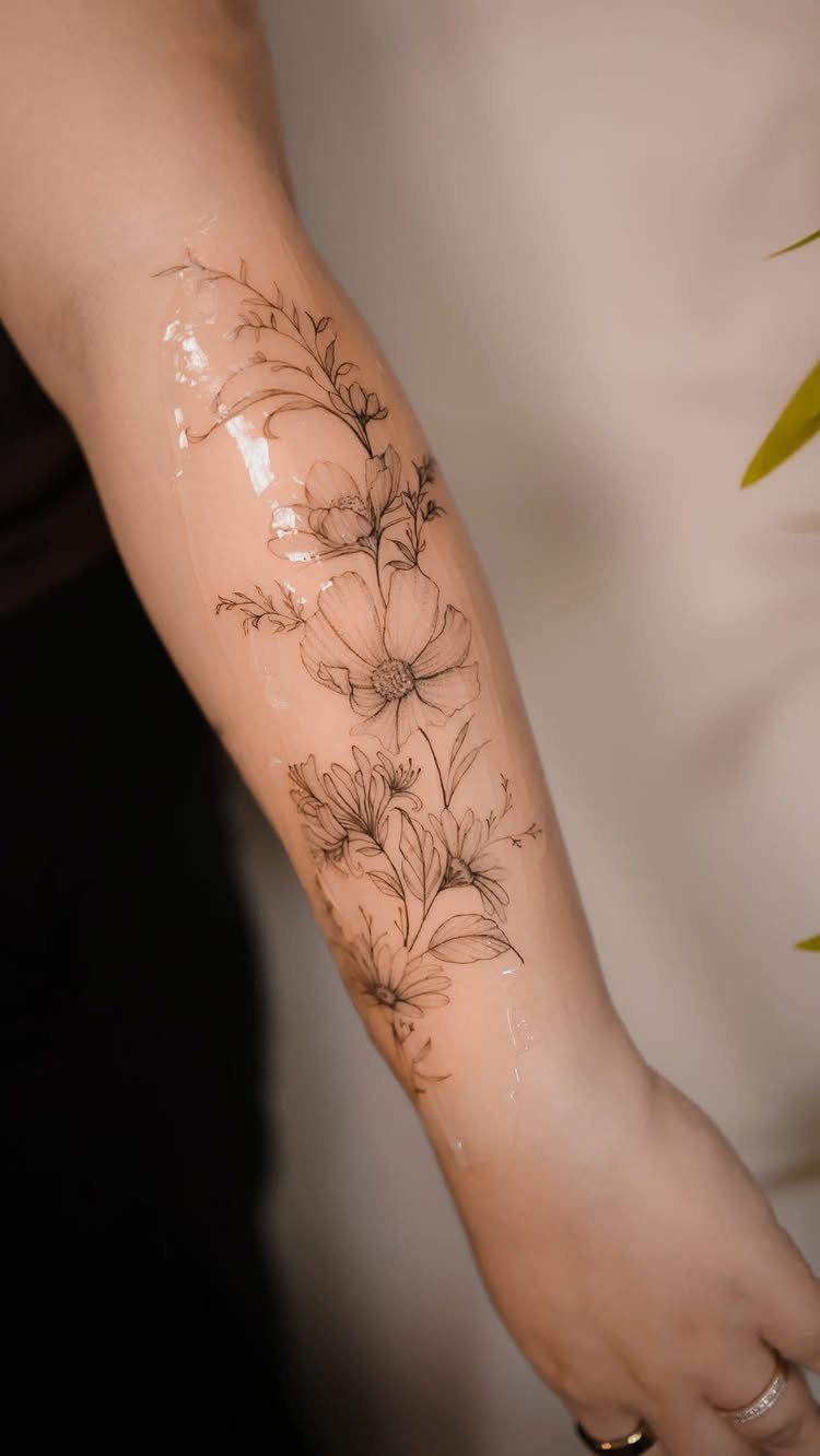 Fine line floral tattoo on a forearm with glossy healing ointment applied