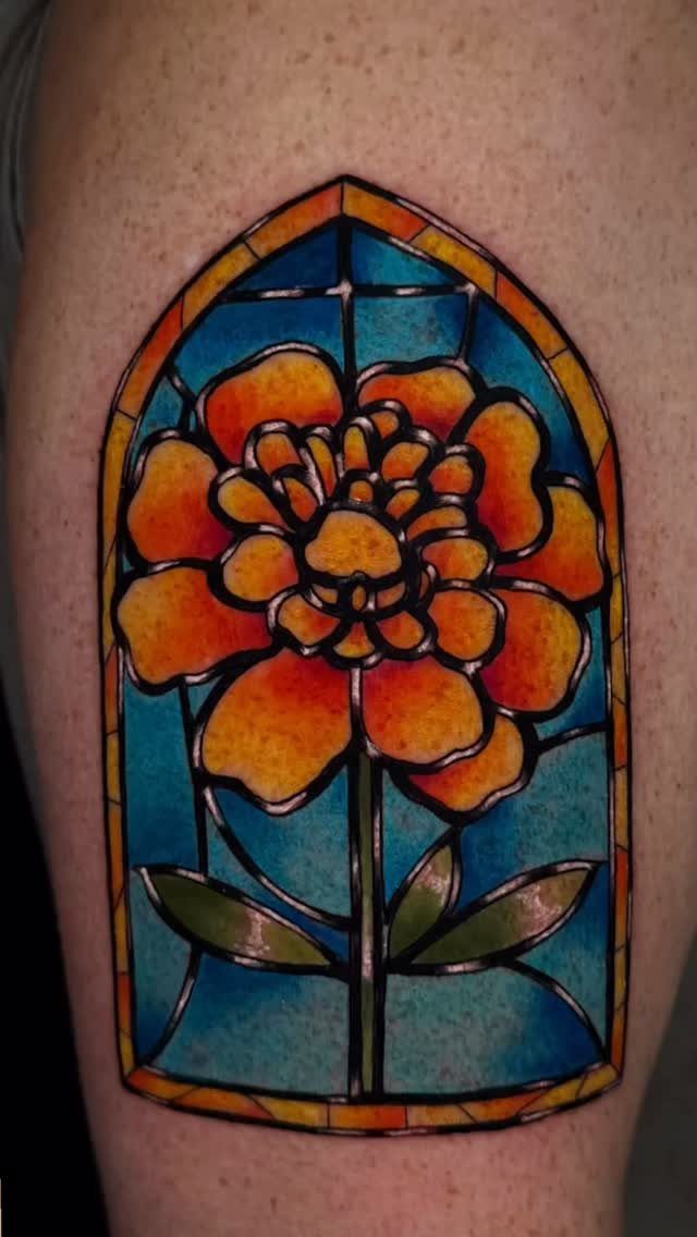 Marigold flower tattoo designed as a colorful stained glass window on skin.