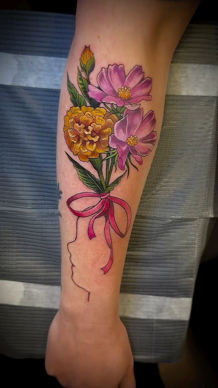 Colorful cosmos and marigold bouquet tattoo with a minimalist face profile on forearm
