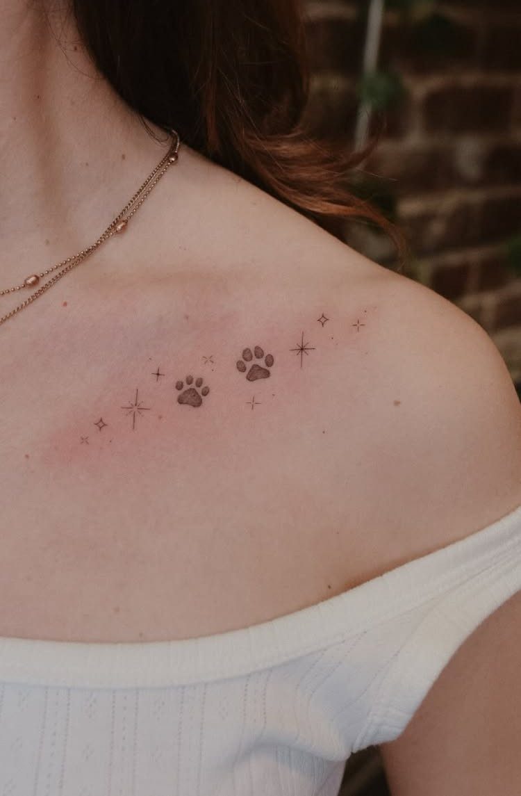 Two small black paw print tattoos with stars on a person's shoulder