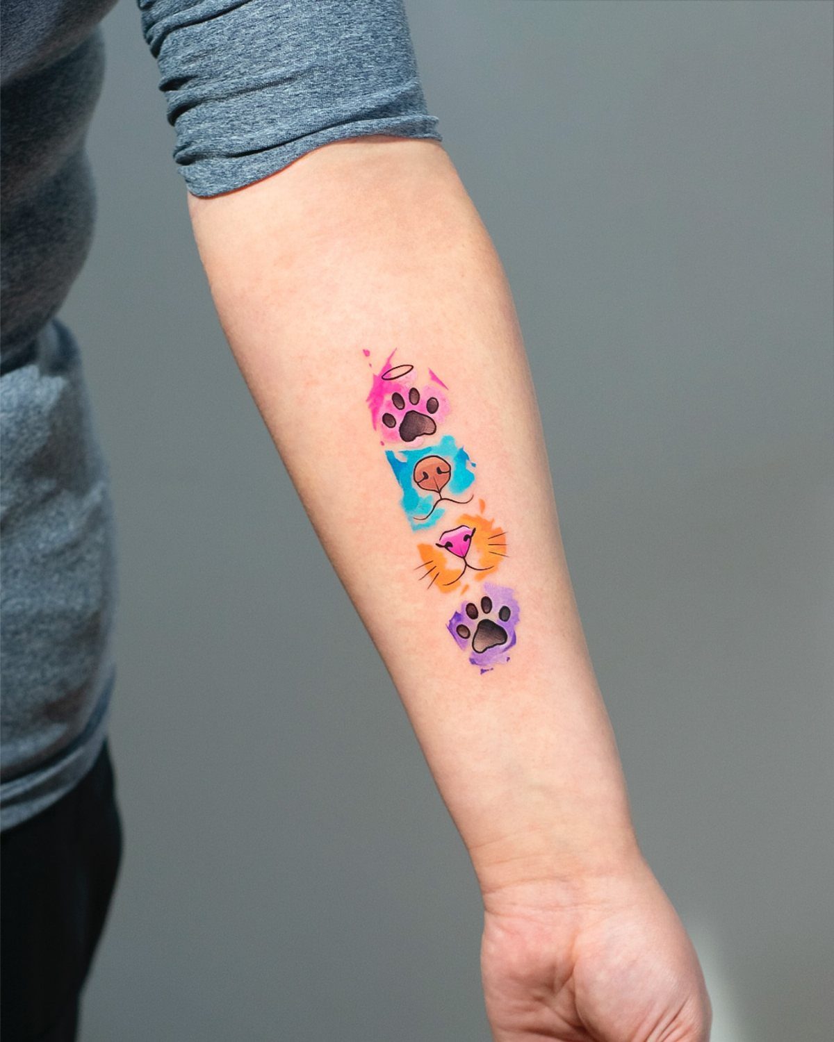 Colorful paw print tattoos in a vertical row on a person's forearm.